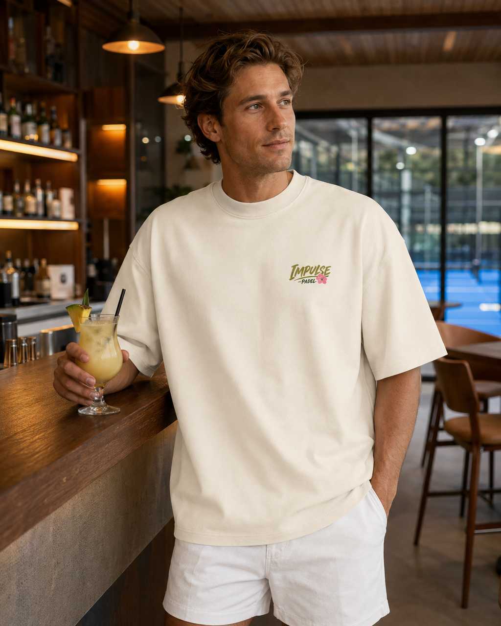 T-shirt homme oversize Padel & Cocktail ivoire porté de face au bar d’un club de padel