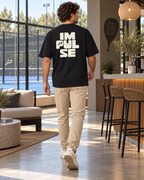 T-shirt homme oversize Impulse noir porté de dos, grand marquage Impulse écru, avec chino beige café